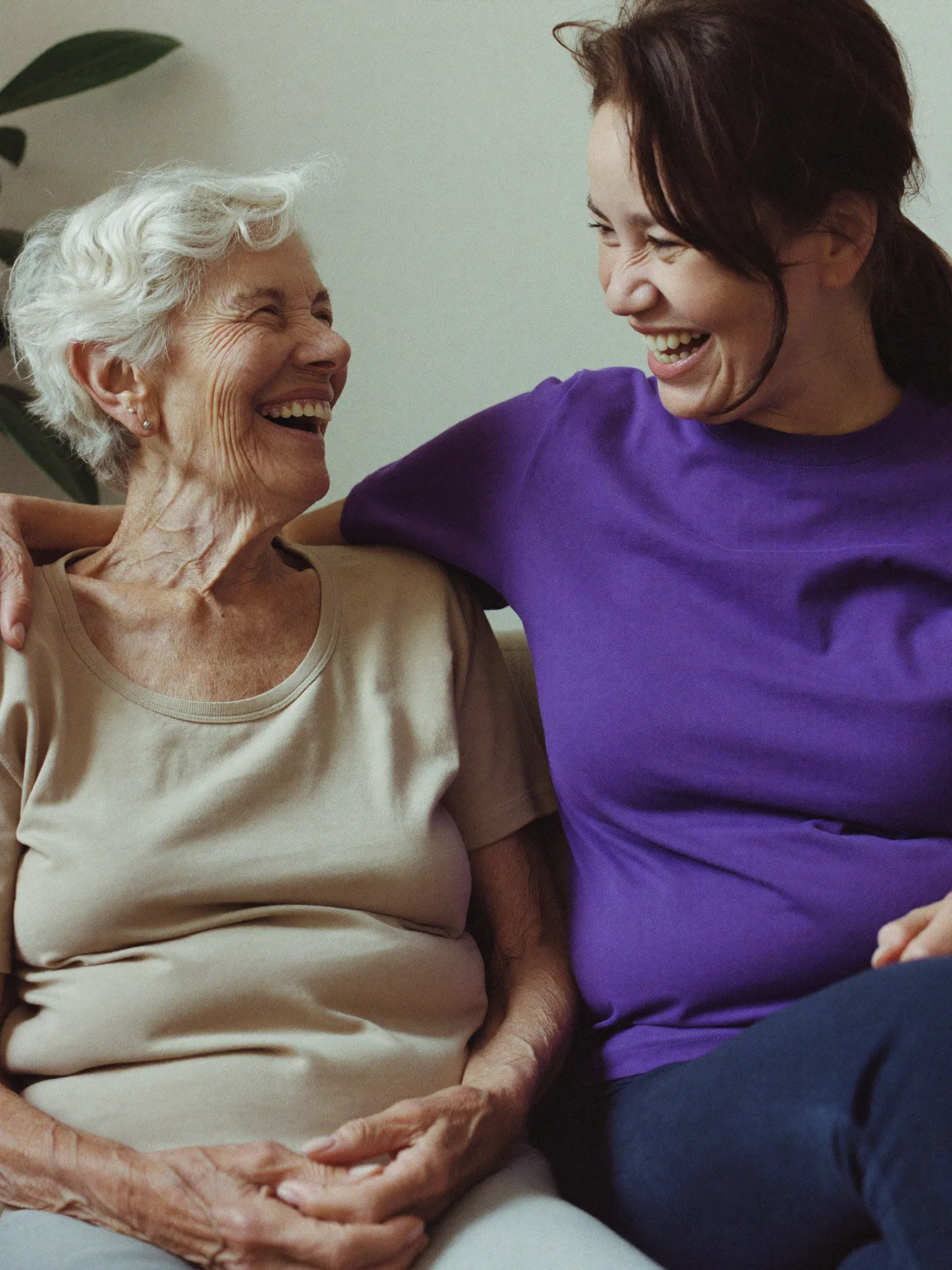 Haushaltshilfe und Seniorin sitzen nebeneinander und lachen